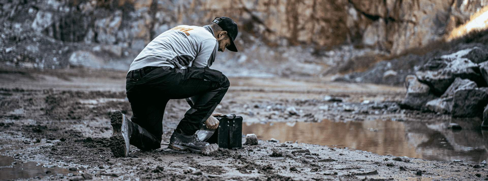 Mann kniet im Schlamm und spannt Ausrüstung in der Nähe einer Pfütze an.