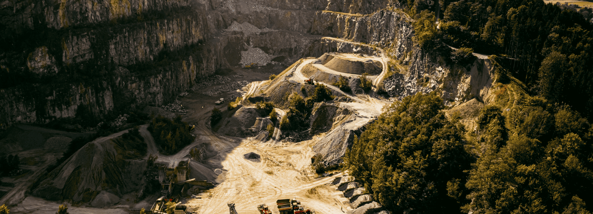 Luftaufnahme eines großen Steinbruchs mit schweren Maschinen und kurvenreichen Straßen.