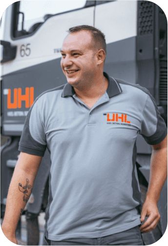 Glücklicher UHL-Mitarbeiter im grauen Arbeitspoloshirt steht neben einem LKW.