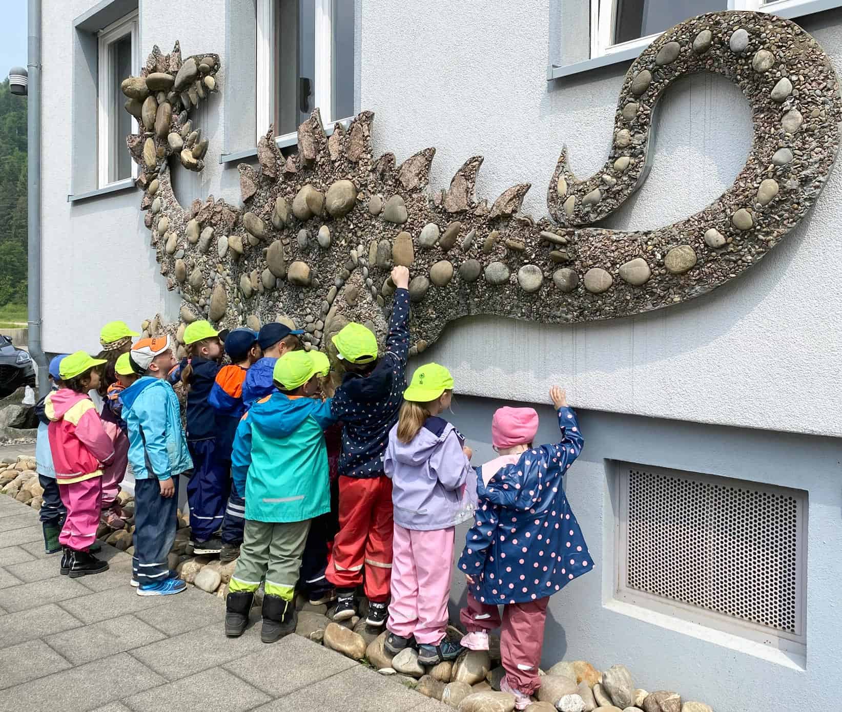 Vorschulkinder bewundern einen großen Mosaikdrachen an einer Hauswand.