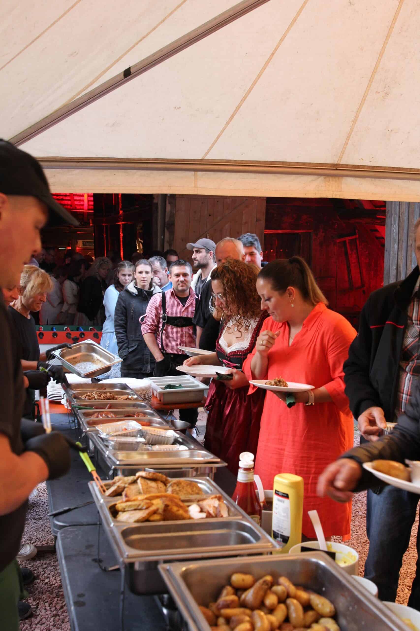 Buffettisch mit verschiedenen Speisen, darunter Bratkartoffeln und Fleisch, bei einer Veranstaltung im Freien.